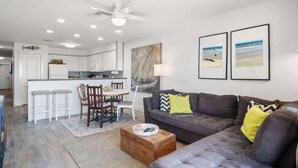 A modern living room with a gray sofa, a wooden coffee table, and a dining area with a white table and chairs. - Ocean Views Boardwalk Access Large Community Pool (Port Aransas)
