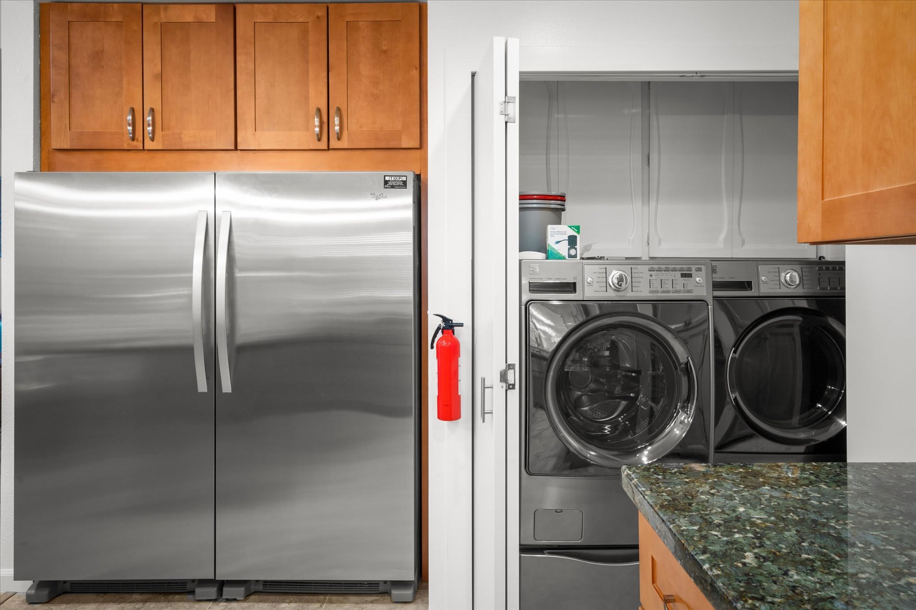 A kitchen with a stainless steel refrigerator, a washing machine, and wooden cabinets.