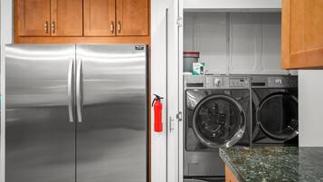 A kitchen with a stainless steel refrigerator, a washing machine, and wooden cabinets.