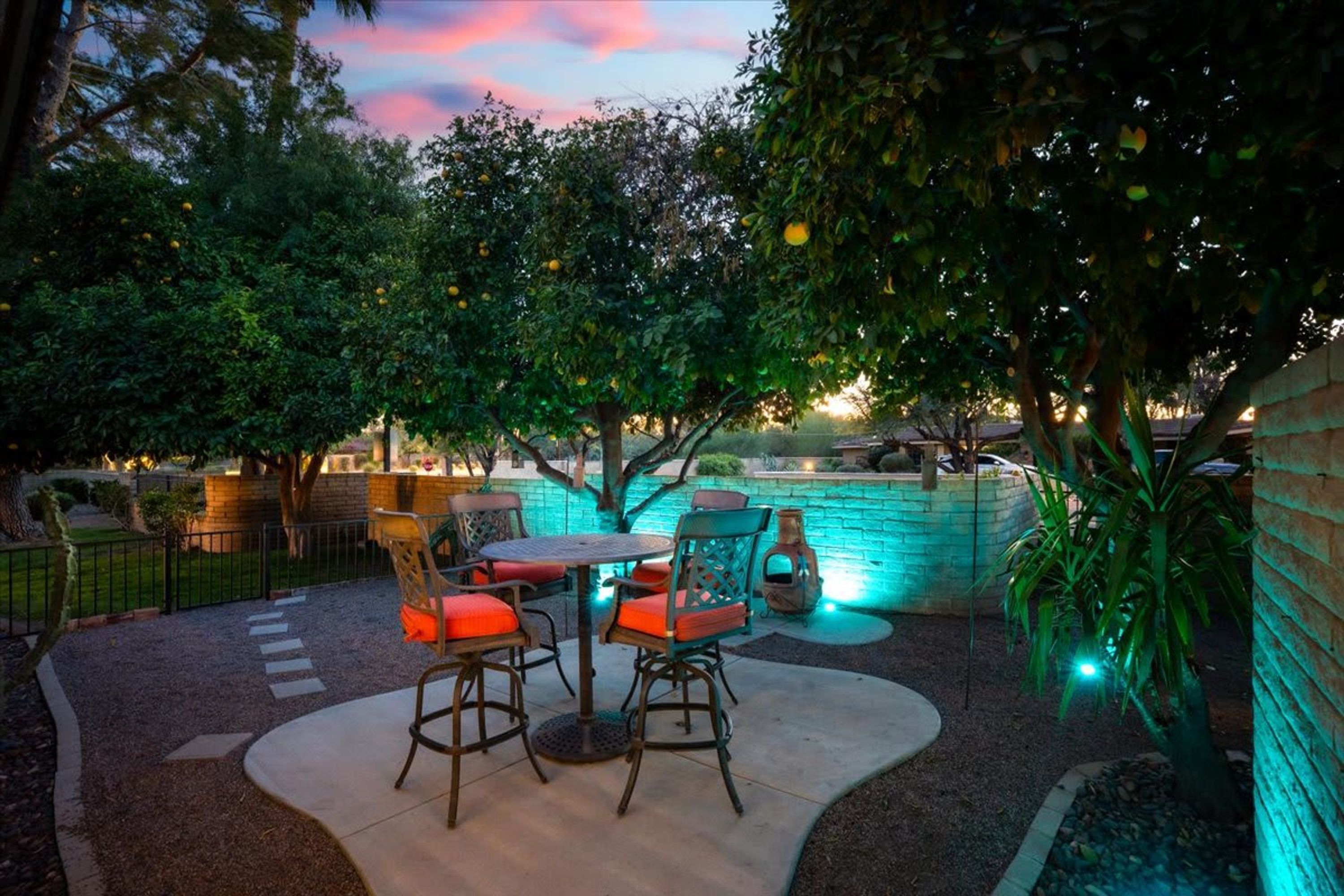 An outdoor patio with a table and chairs, surrounded by trees and a brick wall.