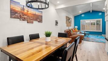 A modern living room with a dining area, featuring a wooden dining table, leather sofas, and a blue accent wall.