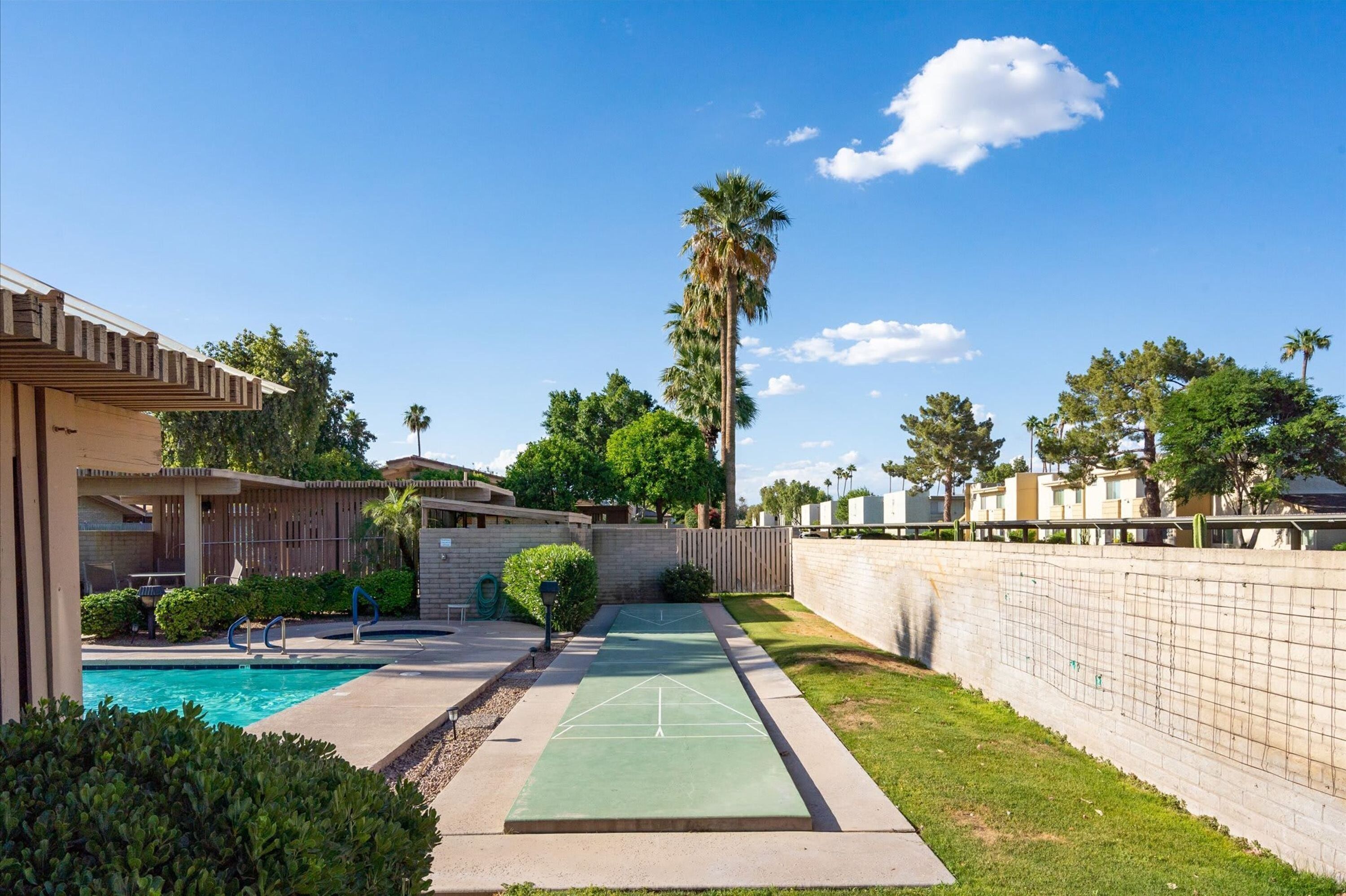 A residential area with a swimming pool, tennis court, and a tall palm tree.