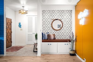 A hallway with a wooden door, a blue wall, a patterned wall, a round mirror, a bench with cushions, and a cactus plant. - Wild Wild West Walk To Old Town 3 Shared Pools (Scottsdale)