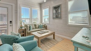 A living room with a sofa set, a coffee table, a ceiling fan, and large windows with blinds. - One Click Away Private Pool EV Charger Beach Toys (Port Aransas)