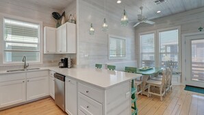 A kitchen with white cabinetry, a central island, a coffee maker, and a dining area with green chairs. - One Click Away Private Pool EV Charger Beach Toys (Port Aransas)