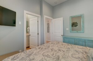 A bedroom with a bed, a dresser, a mirror, and two doors leading to other rooms. - One Click Away Private Pool EV Charger Beach Toys (Port Aransas)