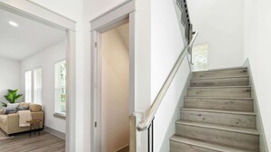 Et moderne interiør med en trappe i træ, en opholdsstue med sofa og en dør, der fører til et andet rum.