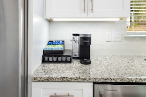 A kitchen with white cabinets, a coffee maker, and a dish rack with blue cups. - 30A Golf Cart Arcade Resort-style Pool (Santa Rosa Beach)