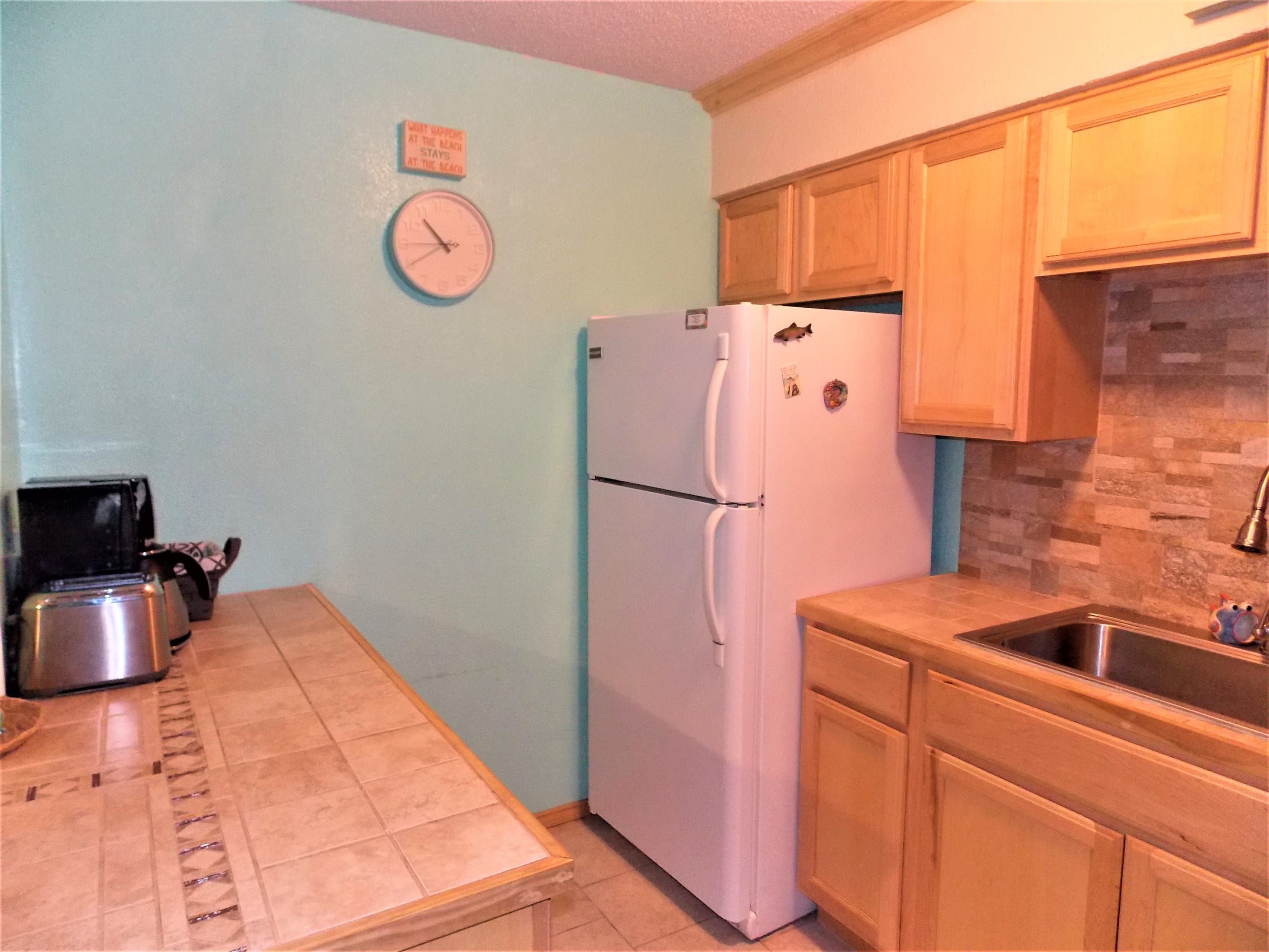 A kitchen with a refrigerator, a clock, wooden cabinets, and a sink.