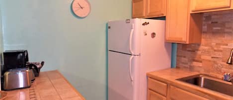Una cocina con refrigerador, un reloj, gabinetes de madera y un lavamanos.