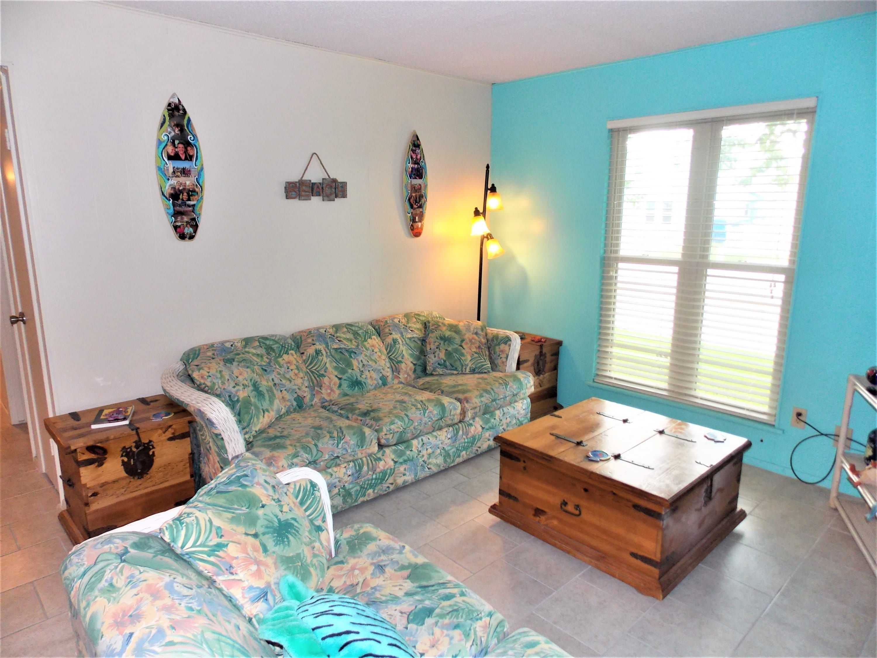 Un salón con un sofá floral, una mesa de centro de madera y una pared decorada con tablas de surf y un cartel que dice 'BEACH'.