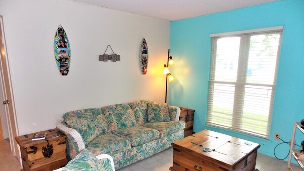 Ein Wohnzimmer mit einem blumigen Sofa, einem Holztisch und einer Wand, die mit Surfbrettern und einem 'BEACH'-Schild dekoriert ist.
