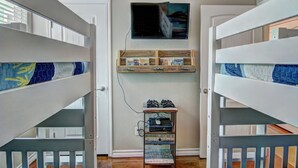 A room with bunk beds, a TV mounted on the wall, and a shelf with items. - Happy Harbor 2 Resort Style Pools Playground (Port Aransas)