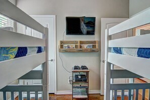 Ein Zimmer mit Etagenbetten, einem an der Wand befestigten Fernseher und einem Regal mit Gegenständen.