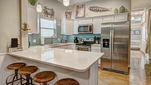 A kitchen with a large island, bar stools, stainless steel appliances, and decorative elements like a fish sculpture and a lighthouse. - Happy Harbor 2 Resort Style Pools Playground (Port Aransas)