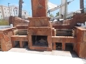 A stone-built outdoor fireplace with a fire burning inside, surrounded by stone steps and walls. - Happy Harbor 2 Resort Style Pools Playground (Port Aransas)