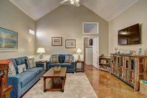 A living room with a high ceiling, a fireplace, a television, and a bookshelf. - Happy Harbor 2 Resort Style Pools Playground (Port Aransas)