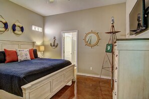 A bedroom with a bed, a door, a wall-mounted mirror, and a wall clock. - Happy Harbor 2 Resort Style Pools Playground (Port Aransas)