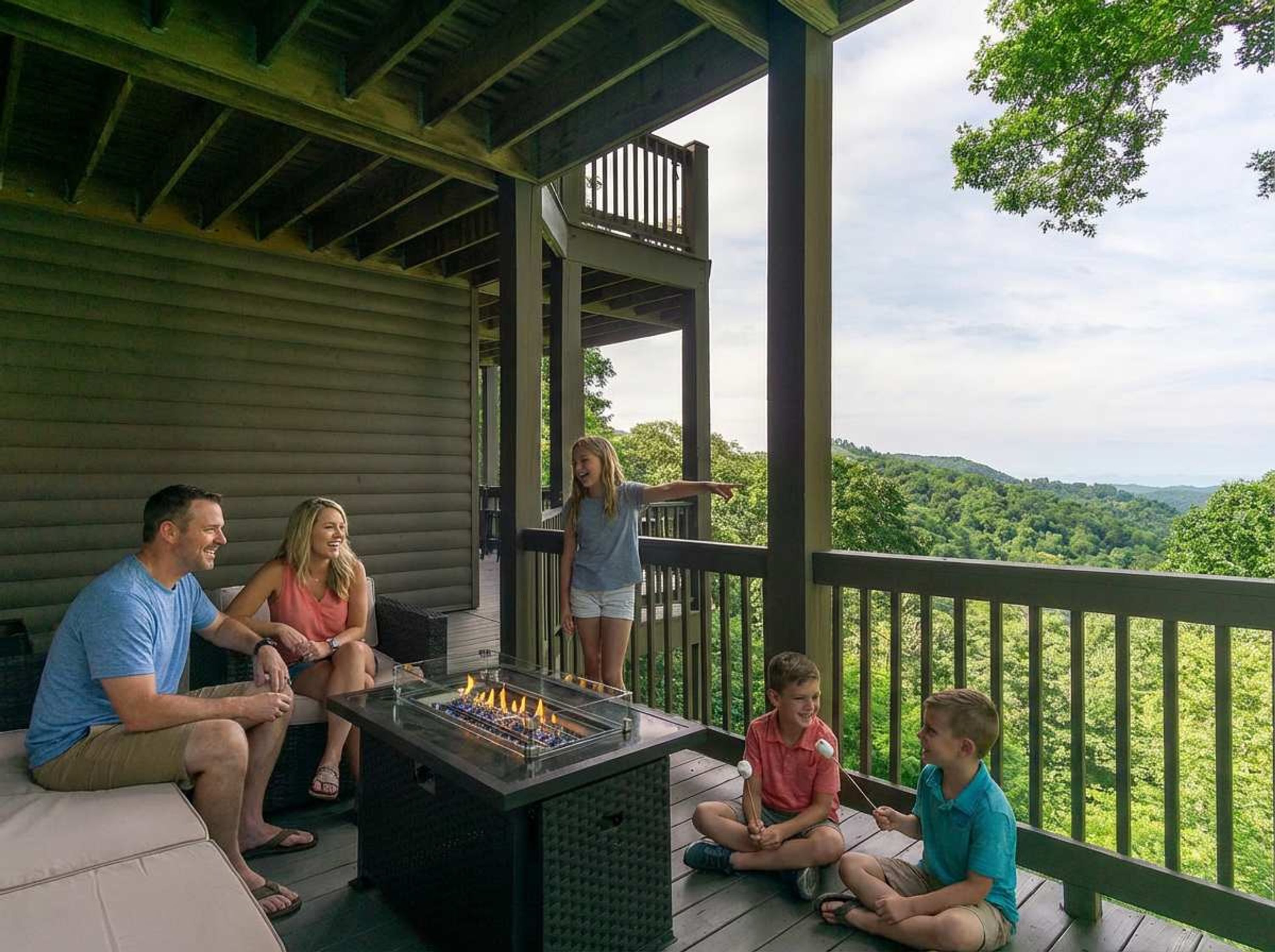 A family on a wooden deck with a fire pit, overlooking a forested landscape.
