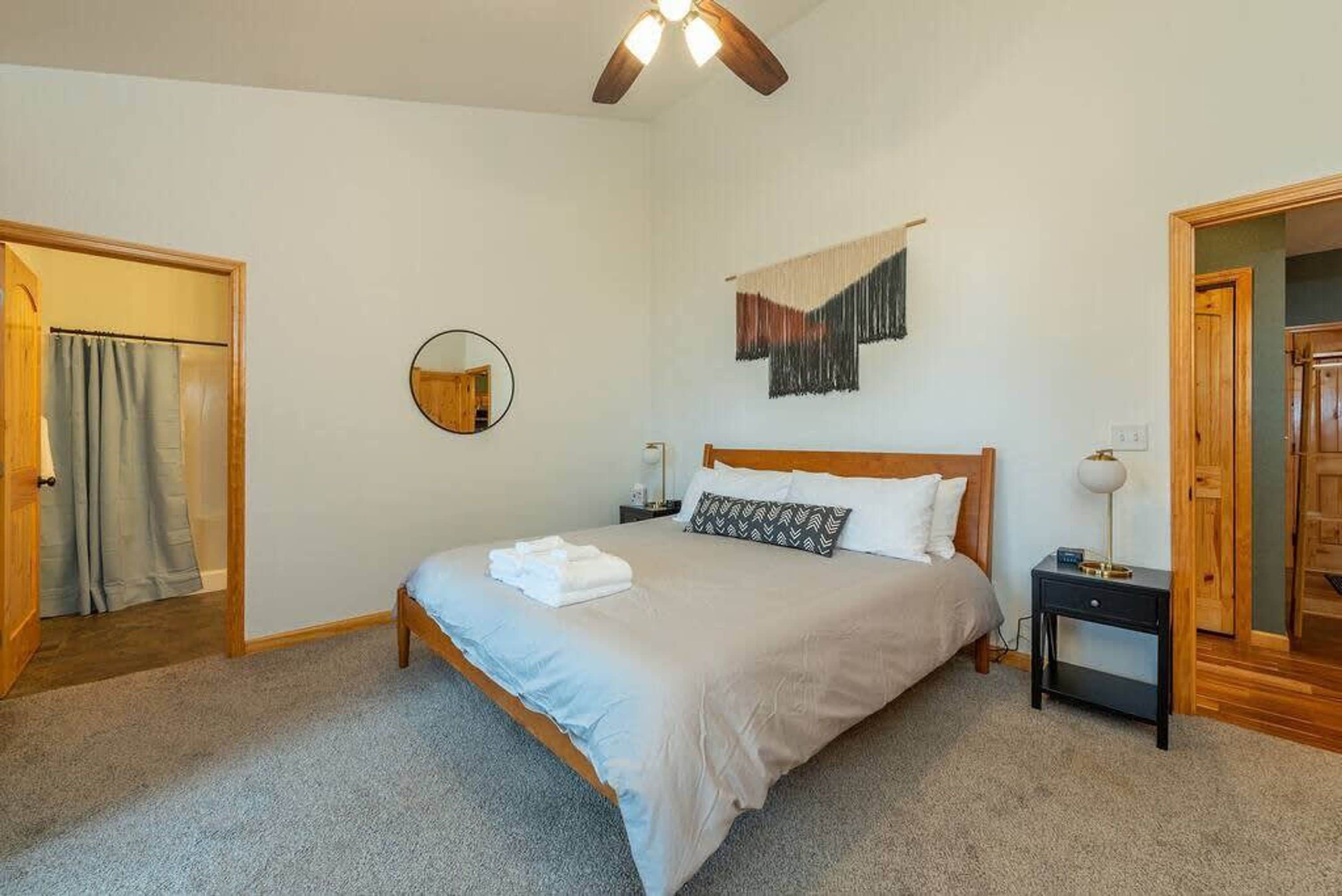 A bedroom with a bed, a round mirror, a bedside table, and a ceiling fan.