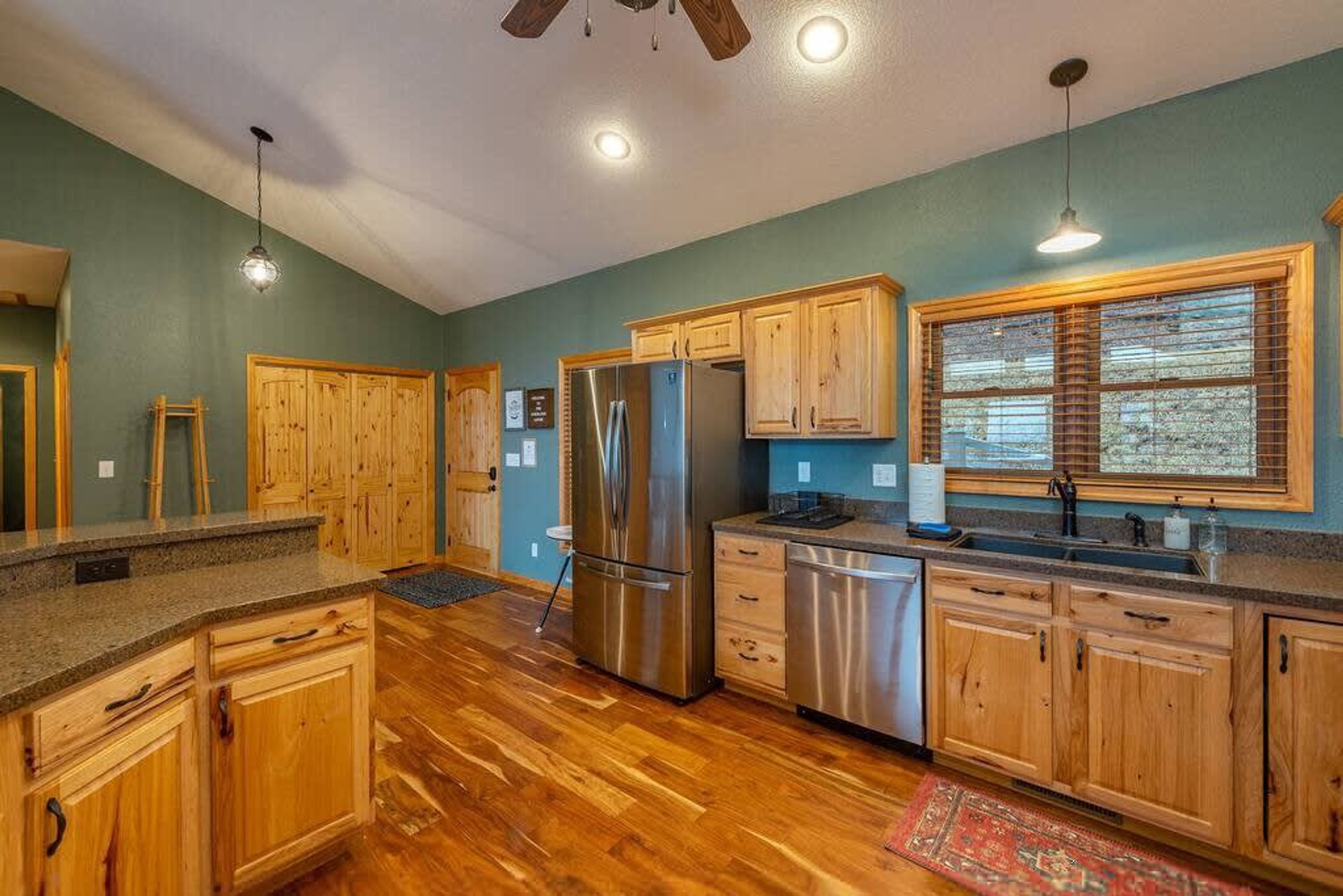A kitchen with wooden cabinets, stainless steel appliances, and a window with blinds.