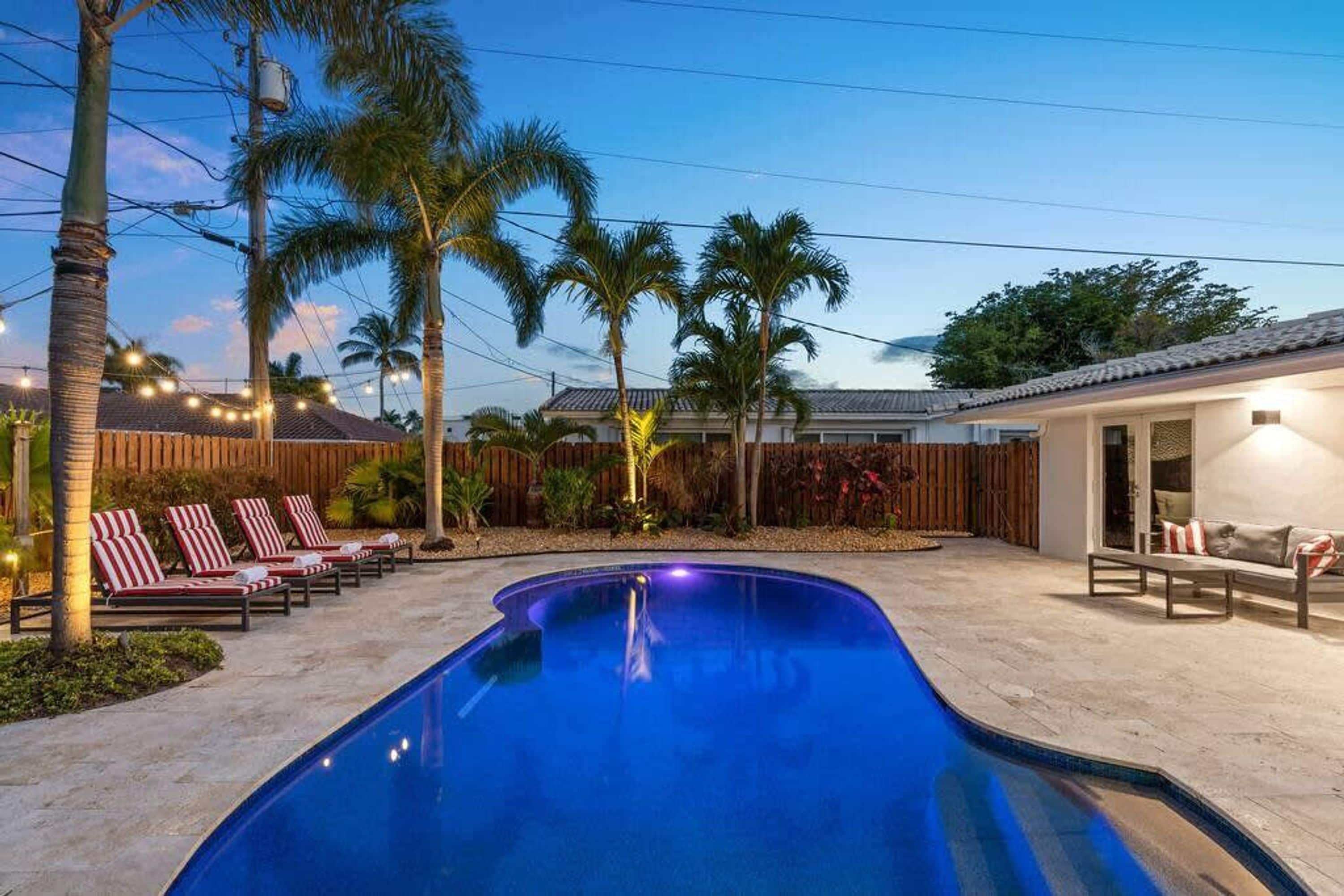 Una piscina con sillones de descanso, palmeras y una valla de madera.