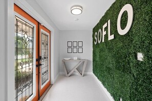 A hallway with a green wall, a white floor, and a door with glass panels. - Heated Pool - Luxury Kitchen - 1 Mile to Beach (Fort Lauderdale)