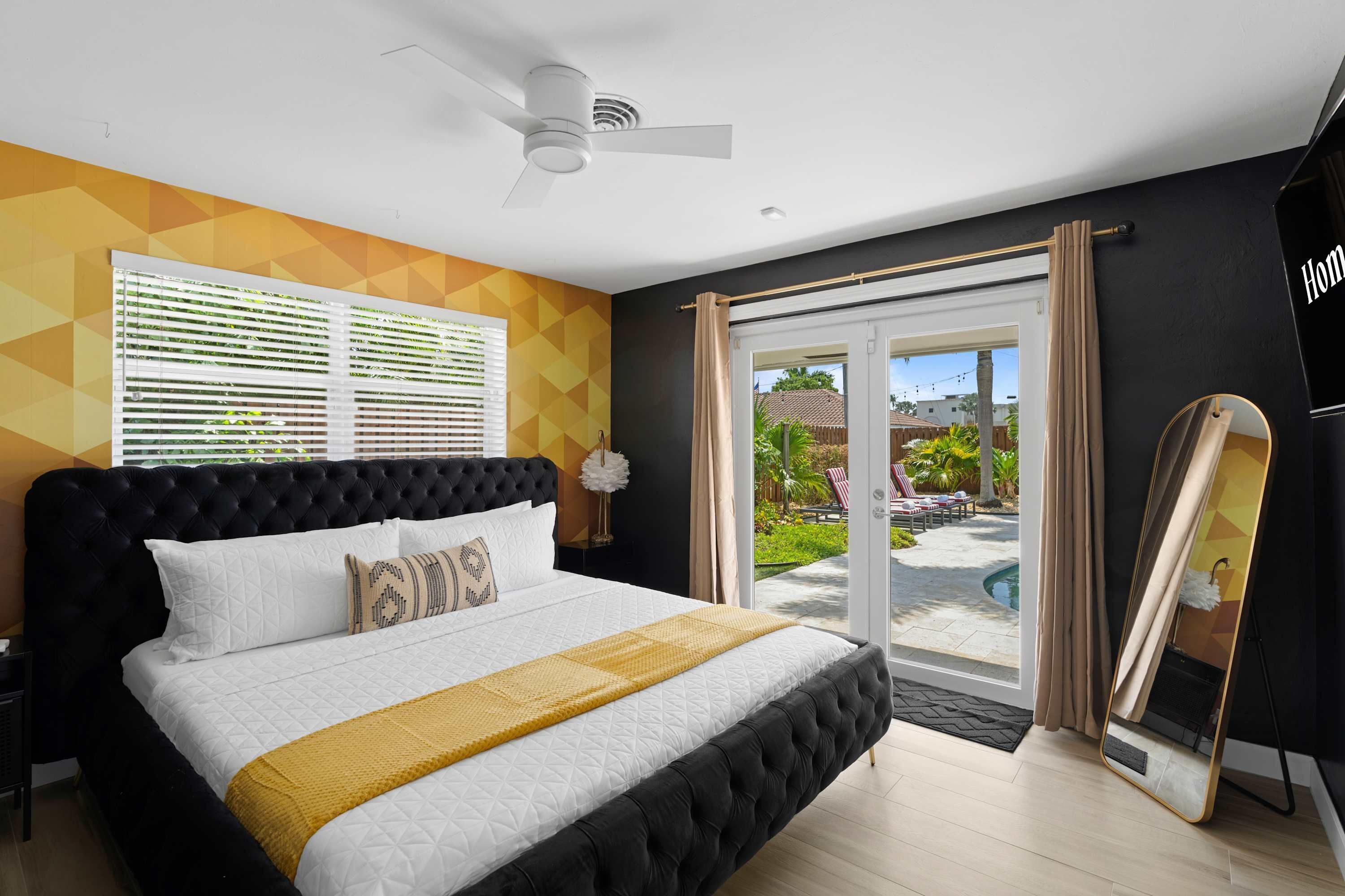 Ein Schlafzimmer mit einem großen Bett, einem Deckenventilator, einem Fenster mit Jalousien und Blick auf einen Pool und einen Außenbereich.
