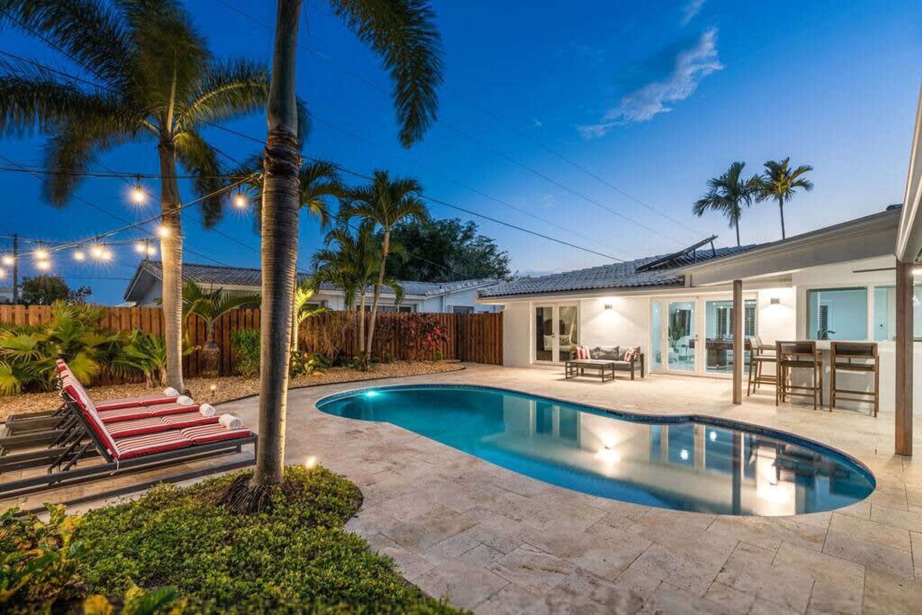 A backyard with a swimming pool, lounge chairs, and a wooden fence.