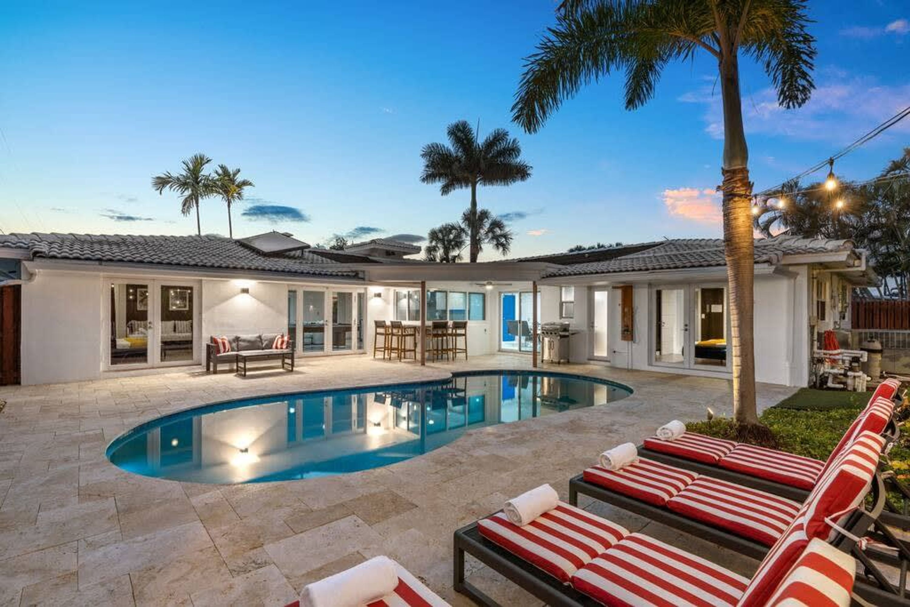 Una propiedad residencial con piscina, mobiliario exterior y palmeras.