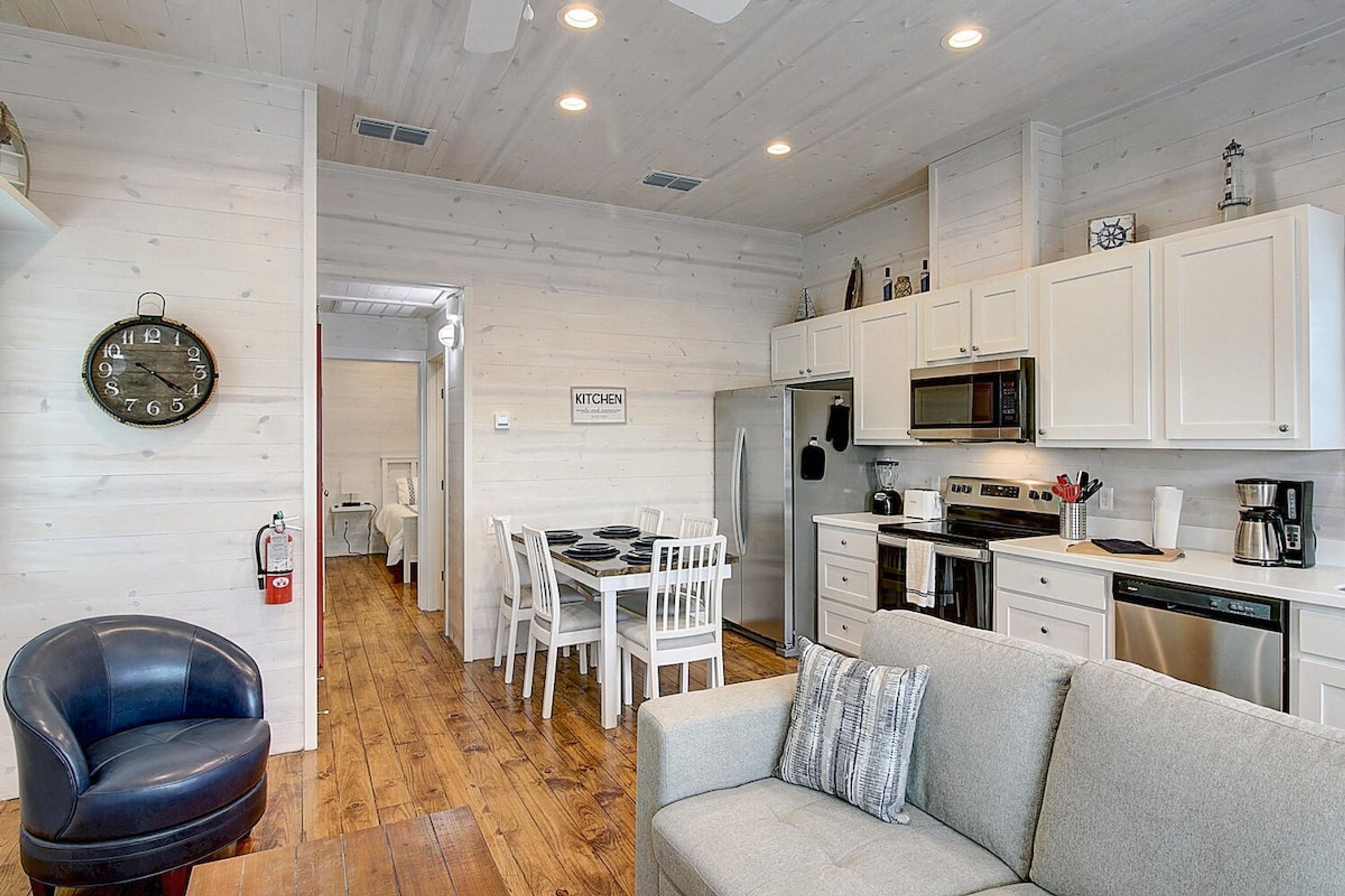 A compact kitchen with white cabinets, a microwave, and a stove. There is a dining area with a table and chairs, and a sofa in the living area.