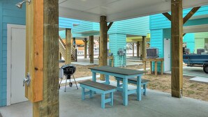 Un patio al aire libre con mesa y bancos de madera, una parrilla y un corredor cubierto con paredes color turquesa.