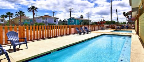 Una piscina con muelle de madera, sillas de descanso y una valla de madera.