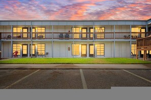 Ein mehrstöckiges Hotel mit schlichter Fassade, Balkonen und einem Parkplatz davor.