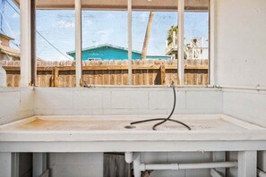 Ein Zimmer mit Fensterblick auf einen umzäunten Bereich, einem weißen Waschbecken und sichtbarer Sanitärinstallation.