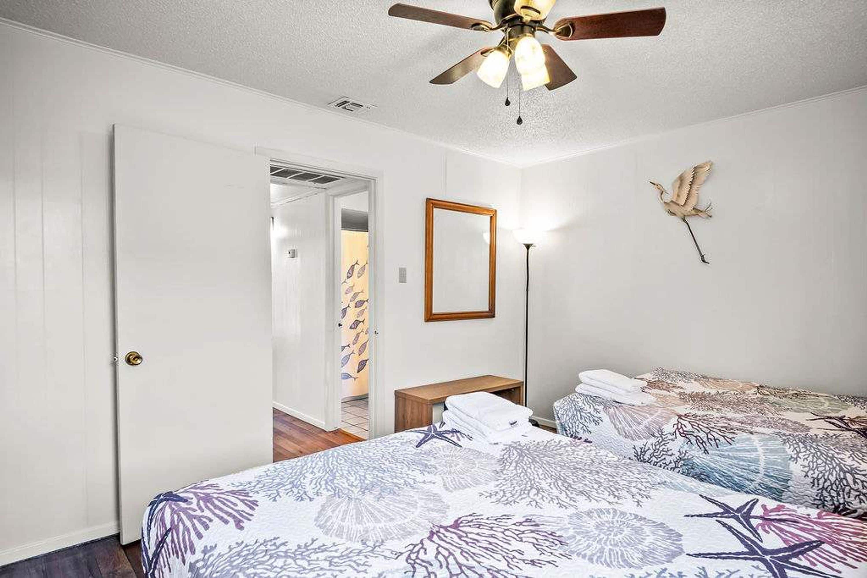 A bedroom with two beds, a ceiling fan, a mirror, and a wall-mounted bird sculpture.