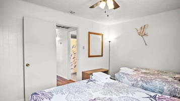 A bedroom with two beds, a ceiling fan, a mirror, and a wall-mounted bird sculpture.