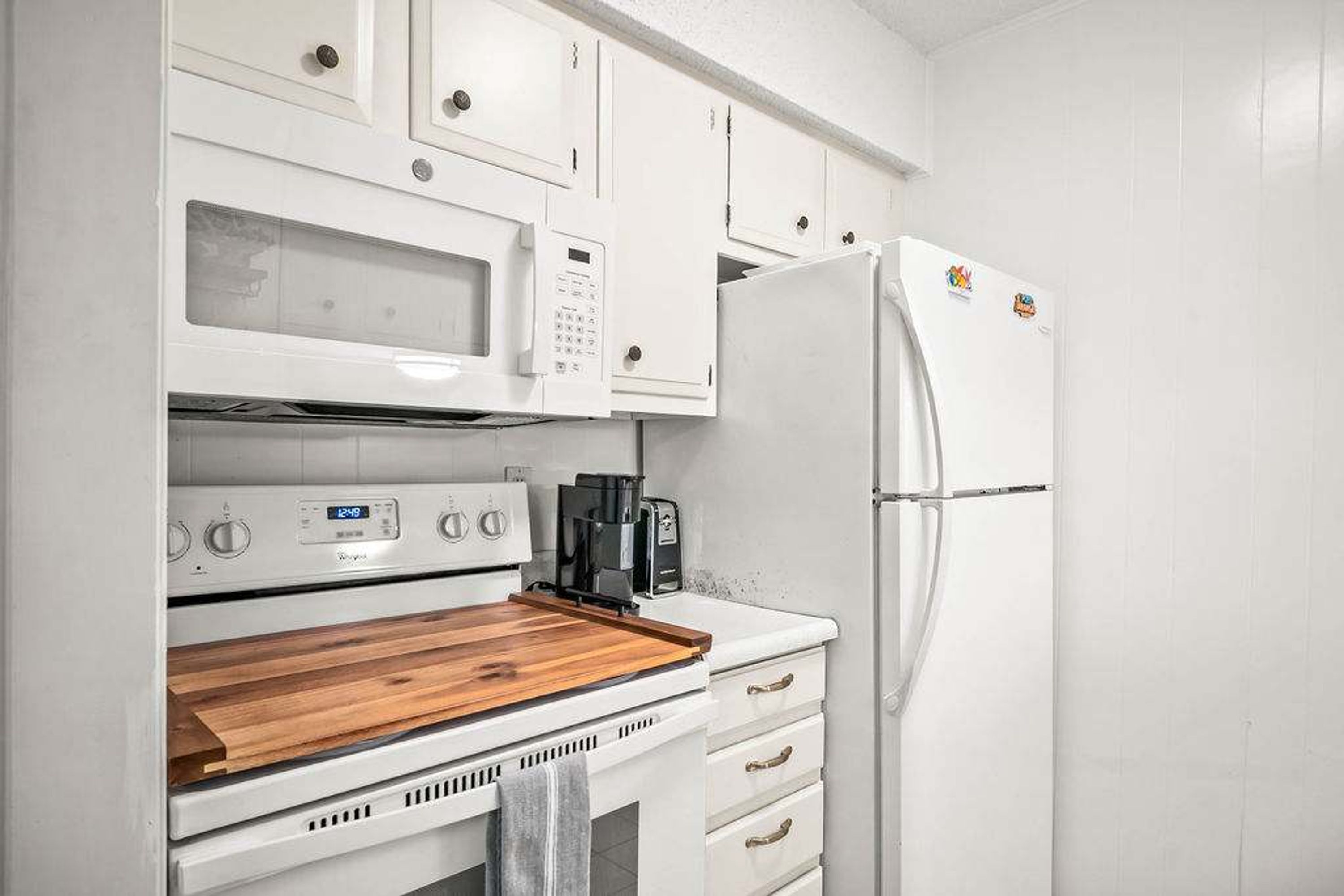 A kitchen with white cabinets, a microwave, a stove, and a refrigerator.