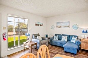Ein Wohnzimmer mit einer Couch, Sesseln, einem Couchtisch und einem Kamin. Ein Fenster bietet Blick ins Freie.