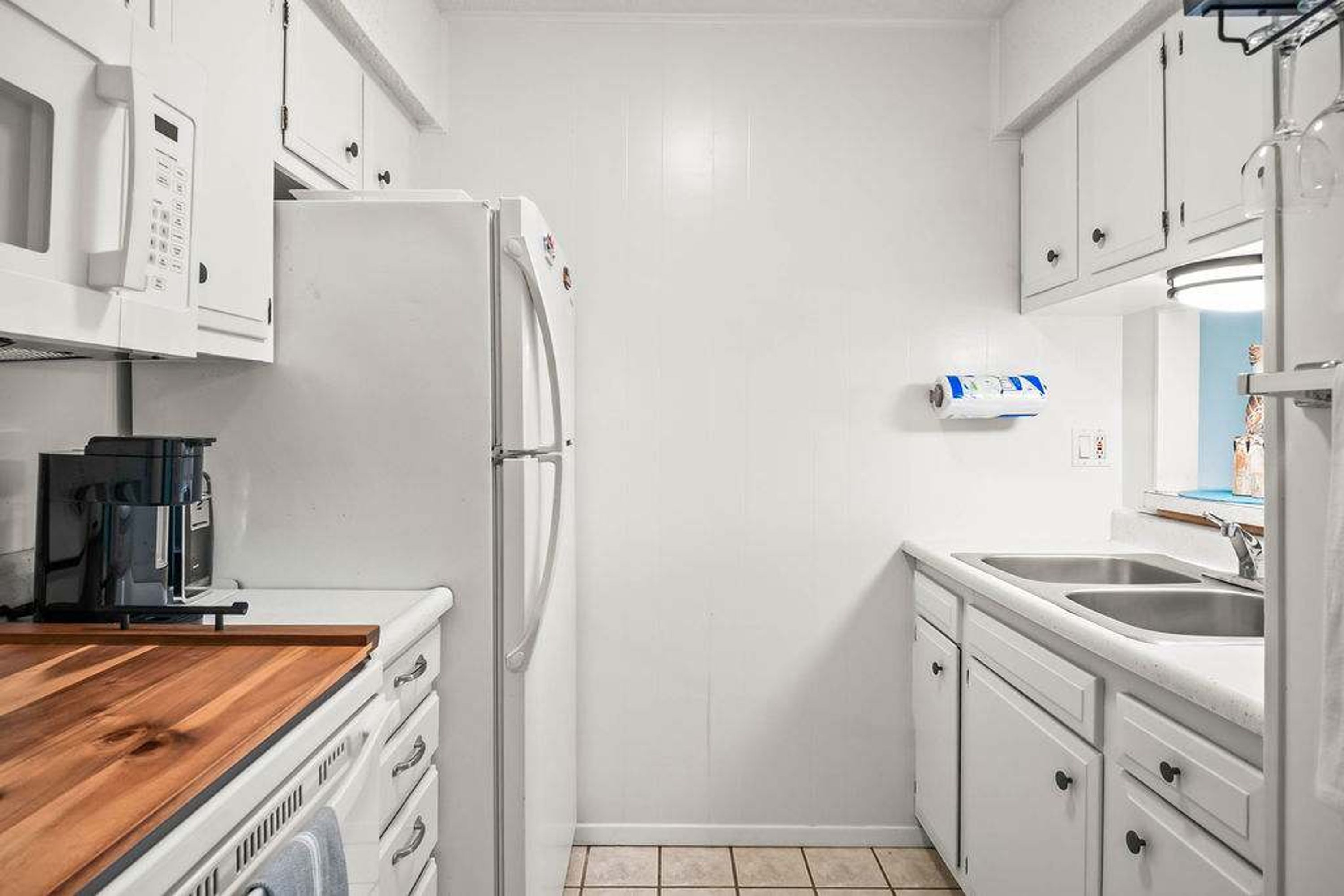 Una cocina compacta con armarios blancos, microondas integrado, cafetera y un lavamanos.