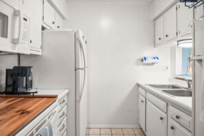 Eine kompakte Küche mit weißen Schränken, einer eingebauten Mikrowelle, einer Kaffeemaschine und einem Spülbecken.
