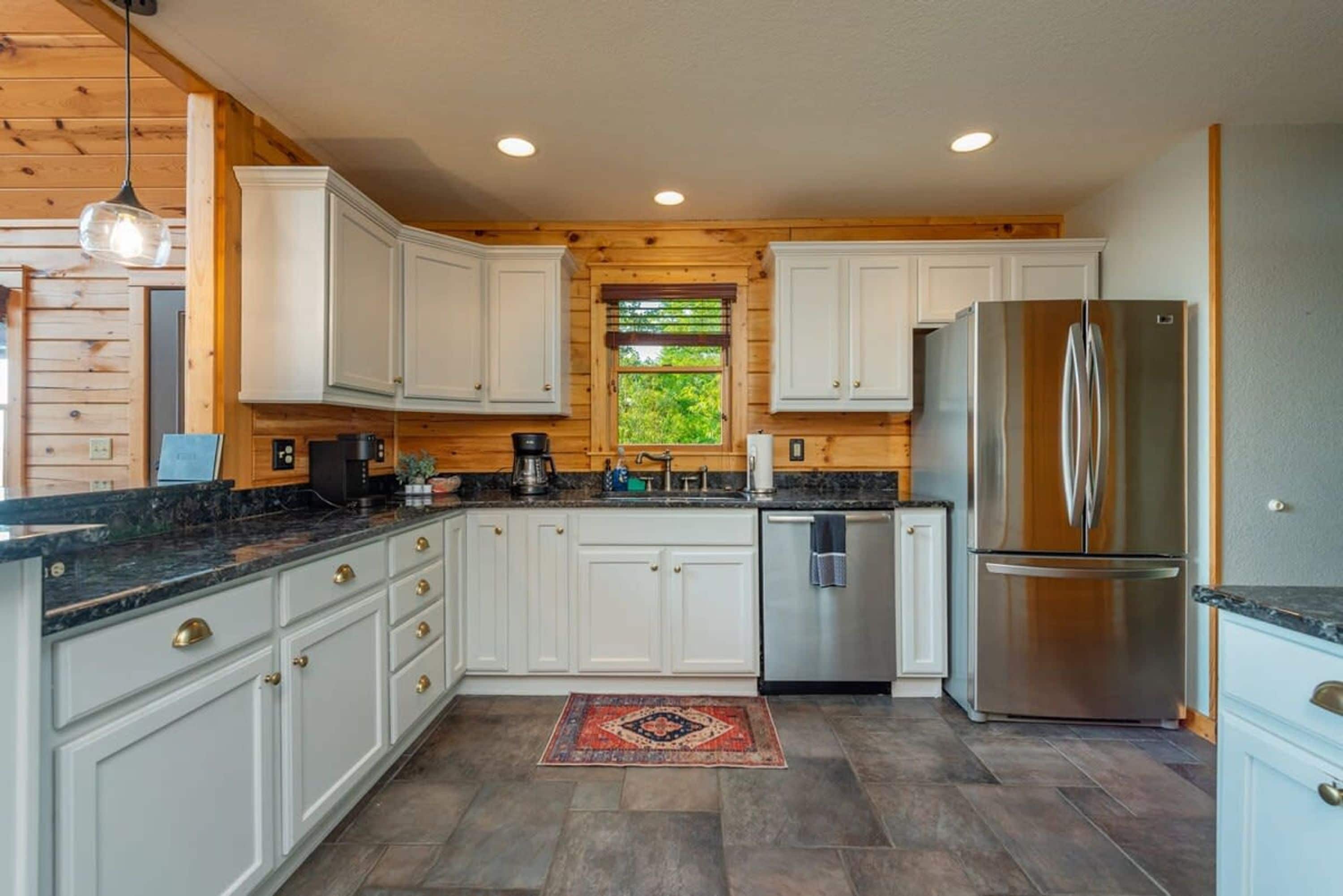 A kitchen with white cabinets, a stainless steel refrigerator, and a window with a view of greenery.
