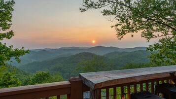 A wooden deck overlooking a mountainous landscape with a sunset.