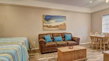 A room with a brown leather sofa, a wooden coffee table, a striped bedspread, and a painting of a landscape.