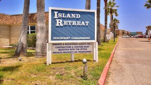 Schild für Island Retreat, das ein Strand-Condominium mit blauem Himmel und Palmen im Hintergrund zeigt.