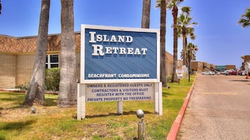A sign for Island Retreat, indicating it is a beachfront condominium with a clear sky and palm trees in the background.