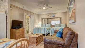 A compact living space with a television, wooden furniture, a ceiling fan, and a bed with striped bedding.