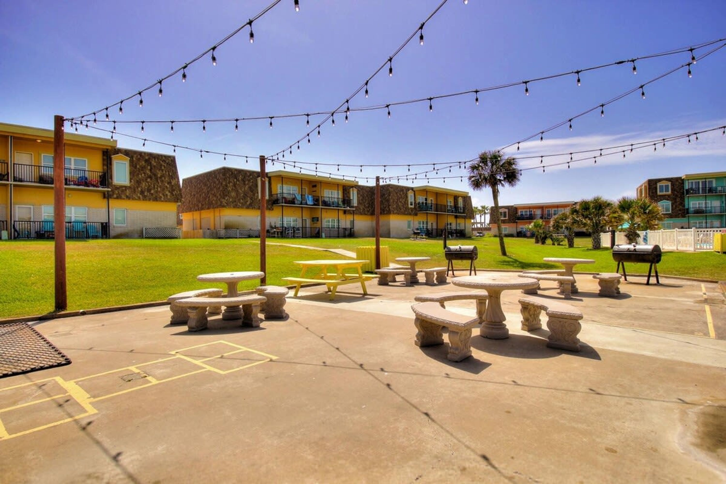 Un patio con mobiliario exterior, una parrilla y luces colgantes.