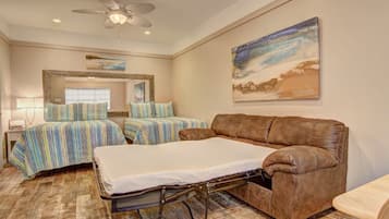 A hotel room with a bed, a sofa, a ceiling fan, and a painting on the wall.