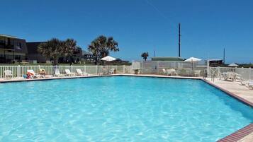 A rectangular swimming pool with a white fence and lounge chairs around it.